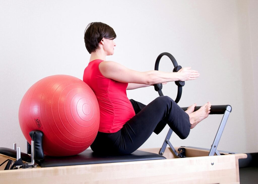 Pregnant woman in gym doing Pilates exercise with reformer and stability ball.